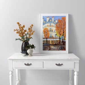 May include: A framed painting of a Parisian street scene with a white building, trees with orange leaves, and bicycles parked on the sidewalk.