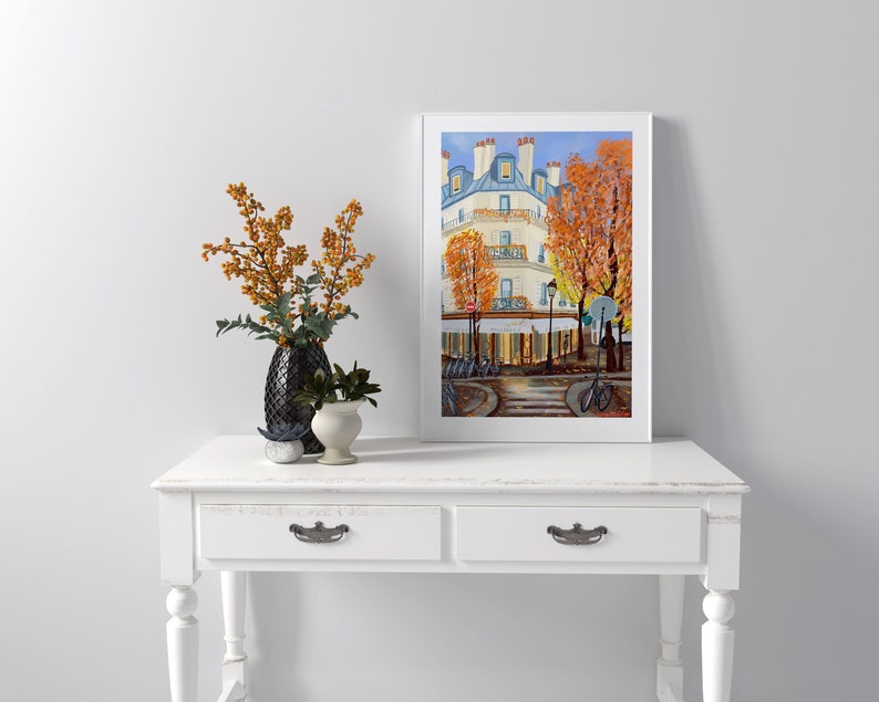 May include: A framed painting of a Parisian street scene with a white building, trees with orange leaves, and bicycles parked on the sidewalk.