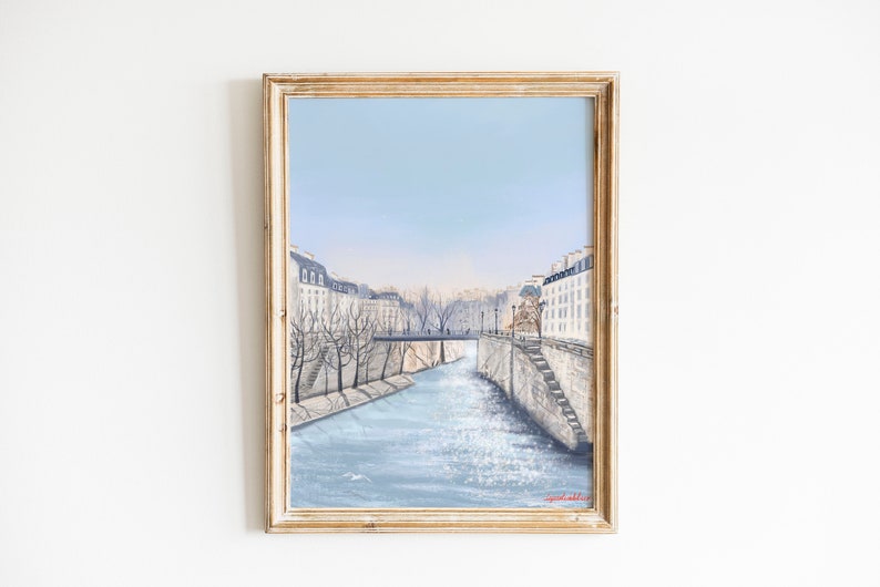 Peut inclure: Une peinture encadr&eacute;e d'un paysage urbain parisien avec un pont au-dessus d'une rivi&egrave;re. Les b&acirc;timents sont blancs avec des toits gris et la rivi&egrave;re est d'un bleu clair. Le ciel est d'un bleu p&acirc;le.