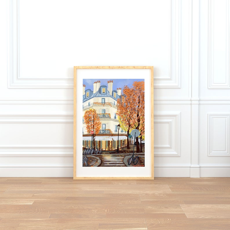May include: A painting of a Parisian street scene with a white building, a cafe, and bicycles. The building has a blue roof and a balcony. The cafe has a sign that says "P&acirc;tisserie". The street is lined with trees with orange leaves.