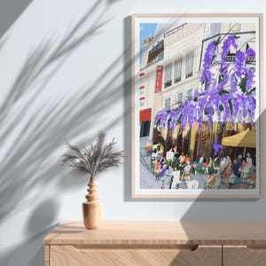 May include: A framed art print depicts a Parisian cafe scene. The artwork showcases a building with a "HOTEL" sign, purple wisteria, and people seated at tables. The print is displayed on a wooden cabinet, with a decorative vase and plant.