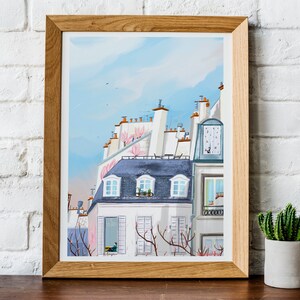 May include: A framed watercolor painting of a Parisian cityscape with a blue sky and pink flowers on the rooftops. The buildings are white with gray slate roofs and windows.
