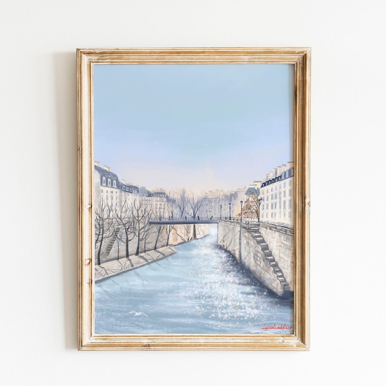 Peut inclure: Une peinture encadr&eacute;e d'un paysage urbain parisien avec une rivi&egrave;re qui le traverse. Les b&acirc;timents sont blancs et la rivi&egrave;re est bleue. Le ciel est bleu clair. La peinture est dans un cadre en bois clair.