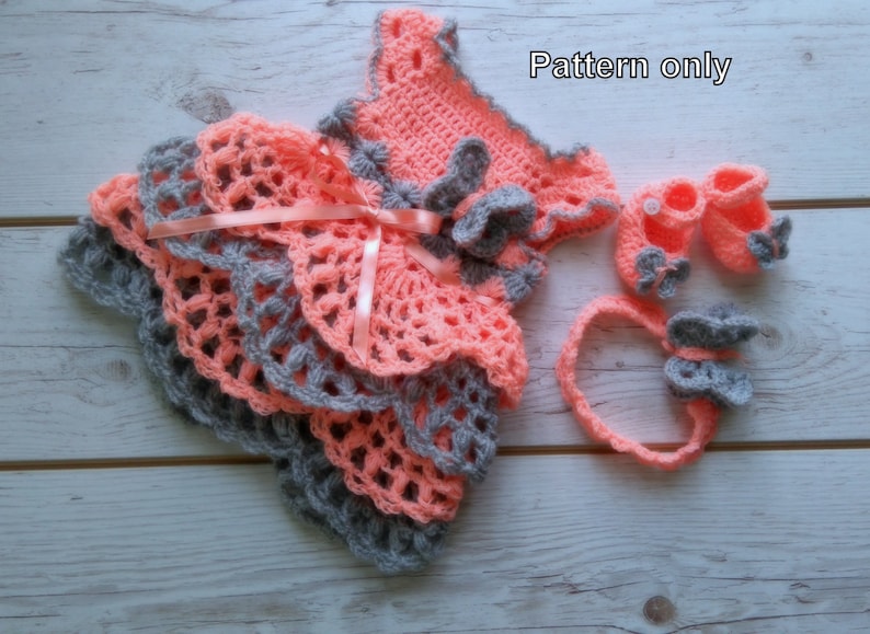 May include: Crochet pattern for a baby dress, headband, and shoes. The dress is pink and gray with a ruffled skirt. The headband and shoes are gray with pink accents. The pattern is for sale, not the finished items.
