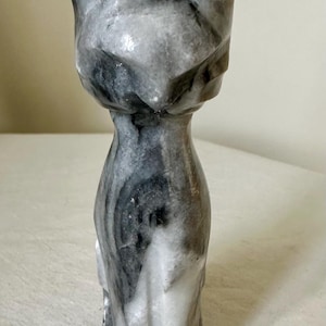 May include: A smooth, polished stone figurine of a cat in a seated position. The sculpture features a marbled pattern with swirling shades of white, gray, and black throughout the entire body, highlighting the natural veining of the stone material.