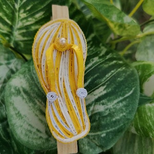 Op de afbeelding: Een gele en witte gestreepte papieren quilling flip-flop met witte parelversieringen.