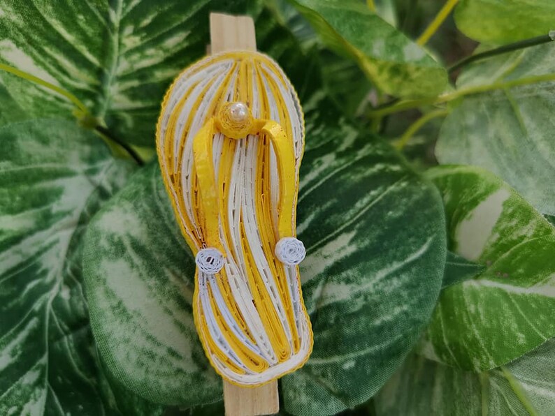 Op de afbeelding: Een gele en witte gestreepte papieren quilling flip-flop met witte parelversieringen.