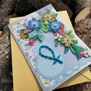 May include: A handmade greeting card with a blue and green paper flower arrangement. The card has a light blue background with a white heart pattern and a white lace border.