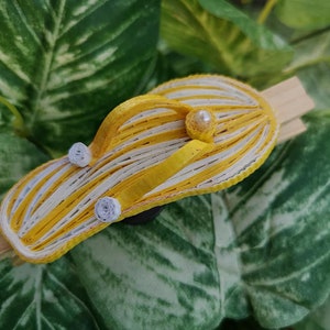 Op de afbeelding: Een gele en witte gestreepte papieren flip-flop met witte parel accenten. De flip-flop is gemaakt van papier en is een knutselproject.