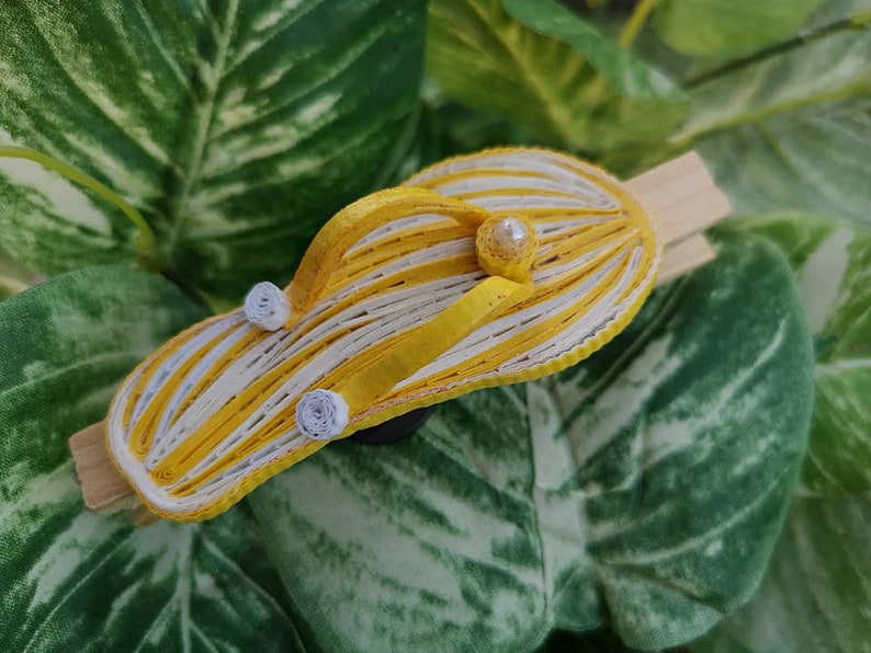 Op de afbeelding: Een gele en witte gestreepte papieren flip-flop met witte parel accenten. De flip-flop is gemaakt van papier en is een knutselproject.