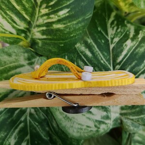 Op de afbeelding: Een gele en witte flip-flop-vormige magneet bevestigd aan een houten wasknijper.