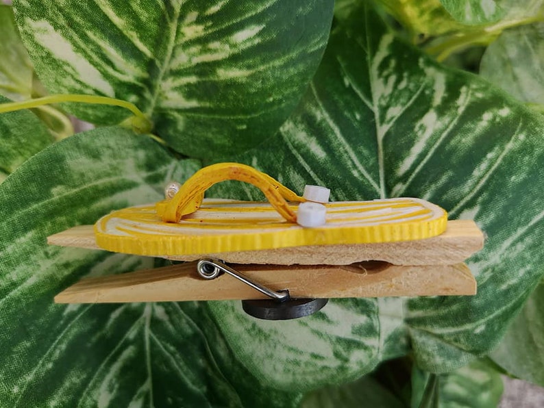 Op de afbeelding: Een gele en witte flip-flop-vormige magneet bevestigd aan een houten wasknijper.