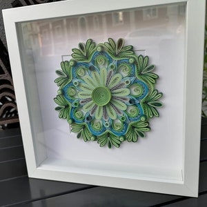 May include: A framed green and blue paper quilling mandala art piece. The mandala is made of paper that has been rolled and shaped into intricate designs.