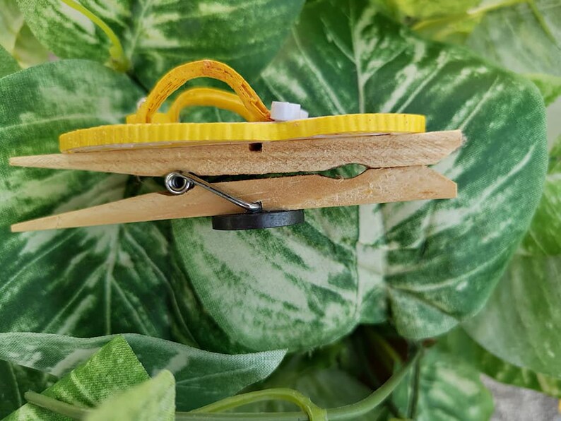 Op de afbeelding: Een gele flip-flop magneet bevestigd aan een houten wasknijper.