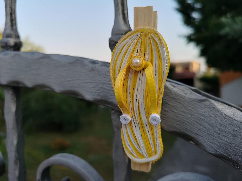 Op de afbeelding: Een gele en witte papieren quilling flip-flop met een parel accent.