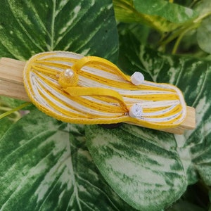 Op de afbeelding: Een gele en witte gestreepte papieren flip-flop met witte parel accenten, bevestigd aan een houten wasknijper.