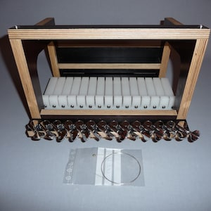 May include: A wooden soap cutter with a black base and white dividers. The cutter has silver knobs and a clear bag with wire. The frame is made of light-coloured wood. The cutter is designed for cutting soap.