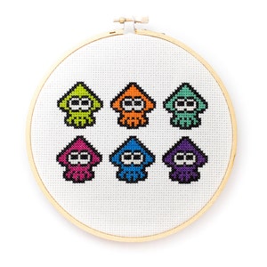 May include: A white embroidery hoop with six colorful pixelated squid designs. The squid are in different colors, including green, orange, pink, blue, and purple.