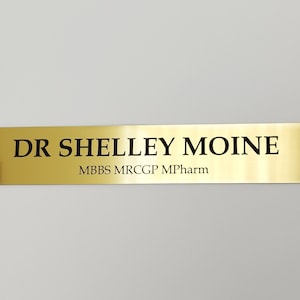 Könnte beinhalten: Goldene Namensschilder mit schwarzem Text, der "DR SHELLEY MOINE" und "MBBS MRCGP MPharm" lautet.