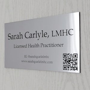 Op de afbeelding: Een zilverkleurig metalen bord met de naam "Sarah Carlyle, LMHC" en de titel "Licensed Health Practitioner" in zwarte tekst. Het bord bevat ook een QR-code en contactgegevens: IG: @sarahqcarlelmhc en www.sarahqcarlelmhc.com.