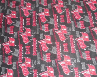 May include: Black fleece fabric with a repeating pattern of the Tampa Bay Buccaneers logo. The logo is red and white with a skull and crossbones and the words "Tampa Bay Buccaneers".