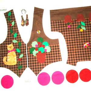May include: Brown plaid vest pieces with felt appliqués of a cat, flowers, and bees. The vest has a brown trim and is decorated with colorful felt circles. The text "POT FULL OF POSIES VEST" is visible.