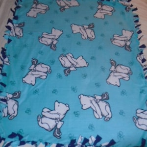 May include: A light blue fleece blanket featuring a repeating pattern of white bears with gray accents. The blanket has a knotted edge in shades of blue and white. The bears are in various poses, and the blanket is suitable for a child's room.
