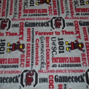 May include: A gray fabric with a repeating pattern of the University of South Carolina Gamecocks logo, mascot, and text. The text includes "Gamecocks", "South Carolina", "University of", "Williams-Brice Stadium", "Fighting Gamecocks", "1801", "SEC", and "Forever to Thee".