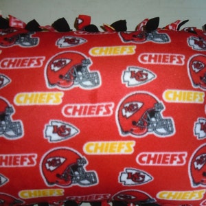 May include: Red and black tie-style fleece pillow with the Kansas City Chiefs logo and the word "Chiefs" repeated throughout the fabric.