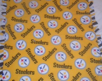 May include: A yellow fleece blanket featuring the word "Steelers" and the team logo in a repeating pattern. The blanket has a fringed edge in black and white. A cozy item for fans.