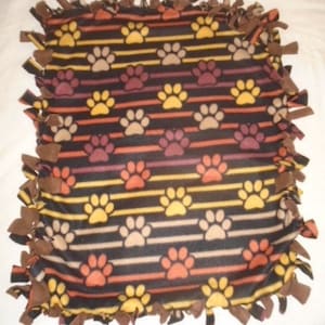 May include: A brown, orange, and yellow fleece tie blanket with a paw print pattern. The blanket is tied with brown fabric knots around the edges.