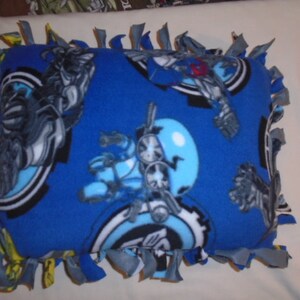 May include: Blue fleece tie pillow with a cartoon character design. The character is wearing a helmet and has a large, round head. The pillow is tied with blue and yellow fabric.
