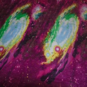 May include: A purple and pink fabric with a galaxy print. The fabric features swirling nebulae with shades of green, blue, and yellow. The background is a dark purple with scattered white stars.