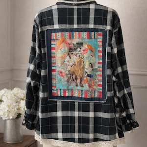 Może przedstawiać: Czarno-biała koszula w kratę zapinana na guziki z dekoracyjną naszywką na plecach. Naszywka przedstawia kolorową ilustrację powozu konnego i postaci. Koszula ma koronkowe wykończenie na dole i kołnierzu.