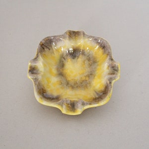 Könnte beinhalten: Ein gelber und brauner Aschenbecher aus Keramik mit einem gewellten Rand.