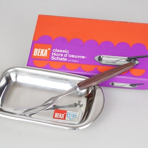 Op de afbeelding: Een zilveren serveerschaal met een vork met houten handvat. De schaal is gelabeld "BEKA classic Hors d'œuvre-Schale mit Gabel".