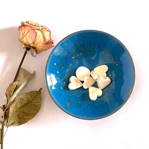 Könnte beinhalten: Eine blaue Keramikschale mit goldenen Akzenten und einem weißen Blumenmuster. Die Schale ist mit weißen herzförmigen Süßigkeiten gefüllt.