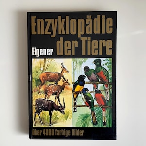 Könnte beinhalten: Ein schwarzes Hardcover-Buch mit dem Titel "Enzyklopädie der Tiere" und goldener Schrift. Das Cover zeigt Illustrationen von Tieren, darunter Hirsche und Vögel. Der Text "über 4000 farbige Bilder" ist ebenfalls sichtbar.