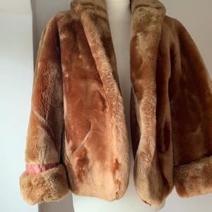 Puede incluir: Un abrigo vintage de piel sint&eacute;tica marr&oacute;n con cuello ancho y pu&ntilde;os. El abrigo se exhibe en un maniqu&iacute;, mostrando su textura afelpada y color c&aacute;lido. Los pu&ntilde;os revelan un forro rosa, agregando un sutil contraste.
