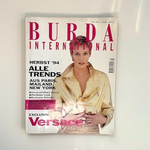 Puede incluir: Una portada de revista con una mujer que lleva una chaqueta de cuero dorada y una falda de lentejuelas. La revista se titula "Burda International" y el texto de la portada dice "Herbst '94 Alle Trends Aus Paris, Mailand, New York" y "Exclusiv: Versace".