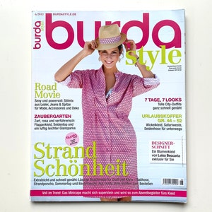 Op de afbeelding: Een tijdschriftcover met een vrouw die een roze en wit gebloemd shirt, een strohoed en een witte ketting draagt. Het tijdschrift heet "Burda Style" en de tekst op de cover luidt: "Road Movie", "Zaubergarten", "Strand Schönheit", "7 Tage, 7 Looks", "Urlaubskoffer", "Designer-Schnitt" en "Voll im Trend: Das Minicape macht sich superklein und wird so zum Abendbegleiter fürs Kleid".