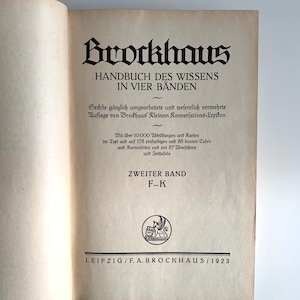 Può includere: Libro aperto con il titolo "Brockhaus HANDBUCH DES WISSENS IN VIER BÄNDEN" in grandi lettere nere ornate. Il testo è in tedesco, con testo aggiuntivo sotto il titolo. Il libro è aperto su una pagina con uno stemma e il testo "ZWEITER BAND F-K" e "LEIPZIG/F.A. BROCKHAUS/1923".