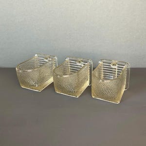 Peut inclure: Trois supports muraux en verre transparent avec une surface texturée. Les supports sont en forme de demi-cercle et ont un petit trou à l'arrière pour la suspension.