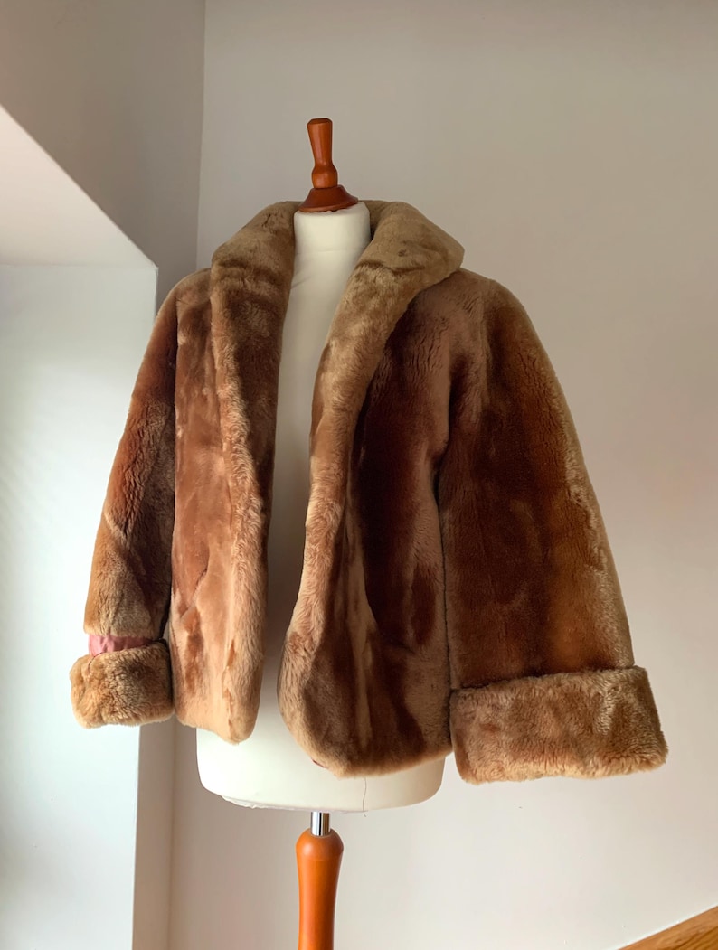 Puede incluir: Chaqueta de piel sint&eacute;tica marr&oacute;n con cuello ancho y pu&ntilde;os. La chaqueta se exhibe en un maniqu&iacute;. Los pu&ntilde;os revelan un toque de forro rosa. La chaqueta es de longitud media.