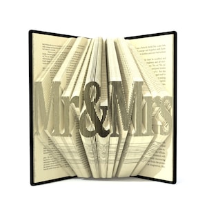 Könnte beinhalten: Ein Buch mit den Worten "Mr. & Mrs." in die Seiten gefaltet. Das Buch ist geöffnet und die Seiten sind aufgefächert, um die Worte zu zeigen.