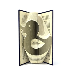 May include: A book with pages folded to create a duck shape. The duck is made of paper and is a light brown colour. The book is open and the duck is protruding from the pages.