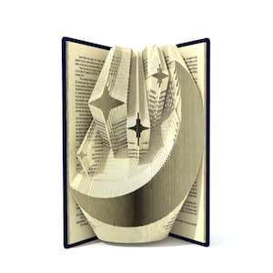 May include: A book with pages folded into the shape of a crescent moon and stars. The book is open and the pages are folded to create a 3D effect.