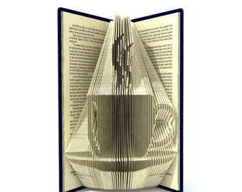 May include: A book with pages folded into the shape of a sailboat. The book is open and the pages are folded to create a three-dimensional sailboat shape. The book is blue and the pages are white.