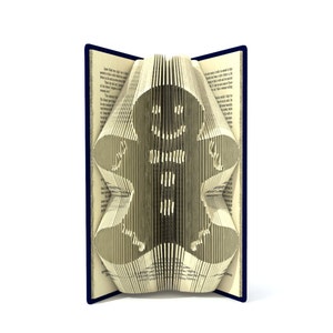 May include: A book with pages folded into the shape of a gingerbread person. The book is open and the gingerbread person is standing upright. The book has a blue cover.