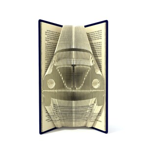 May include: A book with pages folded into the shape of a vintage car. The book is open and the car is standing upright. The book has a dark blue cover.